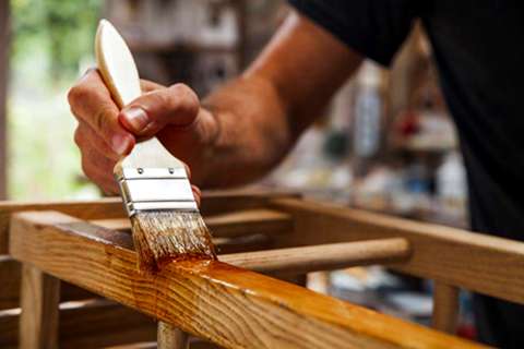 A worker applying varnish to a stool